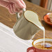 A granite gray stoneware creamer being used to pour milk into a cup of coffee.