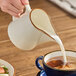A white porcelain creamer is being used to pour milk or cream into a cup of coffee.
