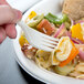 A hand holding a 7 1/8" cornstarch fork over a pasta salad.
