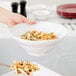 A hand holding a bowl of pasta in an American Metalcraft white melamine bowl.