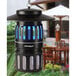 A black Dynatrap bug zapper with blue light hanging from a tree.