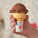 A hand holding a Keebler jacketed cake cone filled with chocolate ice cream.