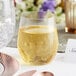 A Visions heavy weight clear plastic stemless wine glass filled with yellow liquid on a table with a place setting.