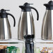 A shelf with three Tablecraft stainless steel coffee carafes.
