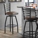 A Lancaster Table & Seating black ladder back bar stool with dark brown vinyl padded seats.