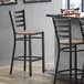 A Lancaster Table & Seating ladder back bar stool with a driftwood seat next to a table.