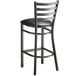 A black metal Lancaster Table & Seating ladder back bar stool with a black vinyl padded seat.