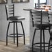 A Lancaster Table & Seating black finish ladder back swivel bar stool with a black vinyl padded seat.