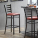 A Lancaster Table & Seating ladder back bar stool with a burgundy vinyl cushion next to a table.