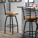 A Lancaster Table & Seating black ladder back swivel bar stool with a light brown cushion.