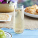 A Choice clear plastic stemless champagne flute filled with champagne on a table with grapes.