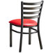 A black metal Lancaster Table & Seating ladder back chair with a red padded seat.