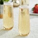 Two Visions clear plastic stemless champagne flutes filled with champagne on a table.