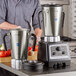 A man in a grey shirt using a silver AvaMix commercial food blender.