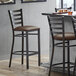 A Lancaster Table & Seating distressed copper ladder back bar stool with dark brown vinyl padded seat.