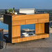 An Astella Indu+ outdoor mobile bistro island with a wood barbecue grill on a stone surface.