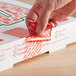 A hand using a red TamperSafe label to seal a white pizza box.