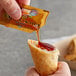 A hand holding a fried egg roll is dipping it into Kikkoman Duck Sauce.