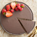 A chocolate pie with a slice missing, topped with strawberries and mint.