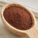 A wooden spoon full of Guittard Grand Cacao Drinking Chocolate powder.