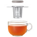 A glass cup of tea with an OXO stainless steel tea infuser basket on top.