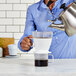 A woman using an OXO pour over coffee dripper to make coffee over a glass cup.