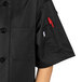 A person wearing a black Uncommon Chef South Beach short sleeve chef coat with a red pocket.