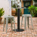 A Lancaster Table & Seating black outdoor table base with stools on a brick patio.