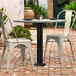 A Lancaster Table & Seating black outdoor table base with a white table and chairs on a brick patio.