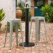 A Lancaster Table & Seating Excalibur black outdoor table base with bar height column on a brick patio with stools.
