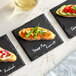 A black square slate coaster with handwritten labeling in white chalk.