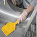 A person in gloves using a yellow Carlisle Sparta nylon paddle blade to clean a metal cylinder.