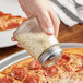 A person sprinkling white cheese on a pepperoni pizza from an American Metalcraft glass cheese shaker.