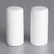 Two white ceramic salt and pepper shakers on a gray surface.