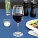 A Libbey wine glass filled with red wine on a table with a salad.