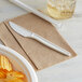 An Eco-Products renewable plant starch knife on a brown napkin next to a plate of potato chips.