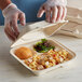 A person in plastic gloves holding an Eco-Products natural compostable 3-compartment paper takeout container of food.