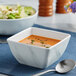 A white square melamine bowl filled with soup with a spoon.
