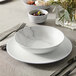 A white American Metalcraft matte round coupe plate with a bowl of olives on a table.