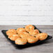 A black GET Milano melamine square plate with pastries on it on a wood table.