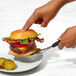 A hand using an OXO stainless steel spatula to touch a burger.