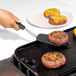 A person using a black OXO flexible spatula to cook burgers on a griddle.