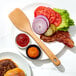 A plate with a hamburger, bacon, lettuce, tomato, and onion with a wooden spatula.