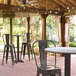 A Lancaster Table & Seating Excalibur bar height table with a textured top on a covered patio.