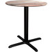 A Lancaster Table & Seating round dining table with a black cross base and wooden top.