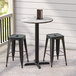 A Lancaster Table & Seating round black table with a cross base plate on an outdoor patio with black stools.