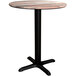 A Lancaster Table & Seating round dining height table with a wooden top and black cross base.