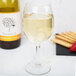 A close up of a Libbey white wine glass full of white wine next to a bottle of white wine with crackers.