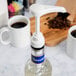 A white Tablecraft coffee syrup pump on a bottle of coffee syrup next to a coffee maker.
