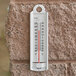 A Taylor wall thermometer on a brick wall with a red line showing the temperature.